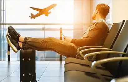 Traveler with feet up on a suitcase as an airliner takes off outside the terminal