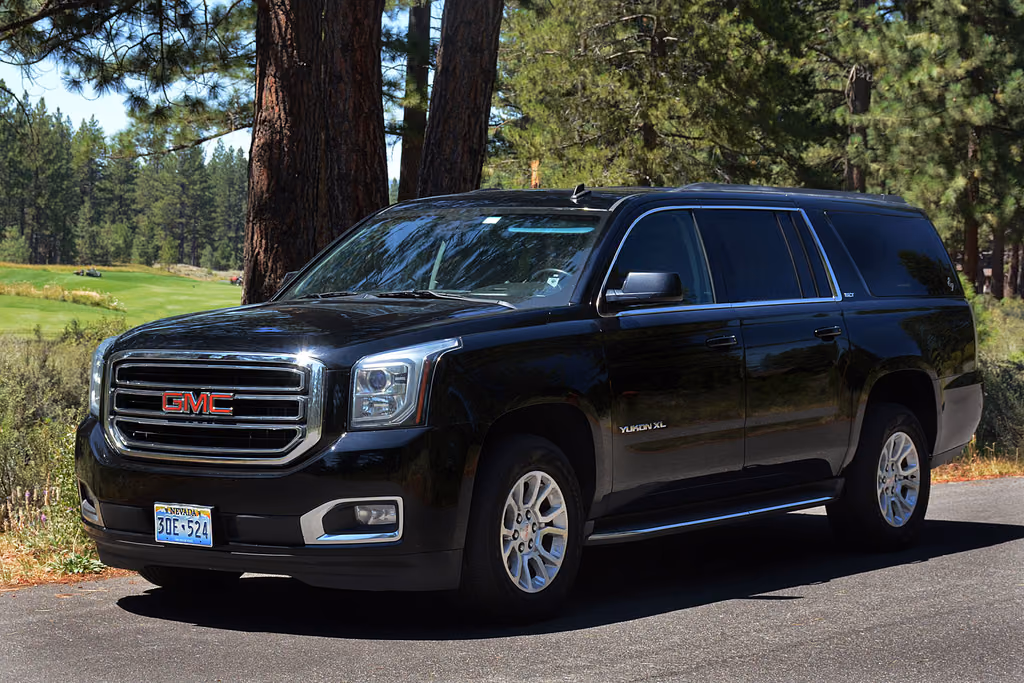 Black GMC Yukon XL SUV parked under tall pine trees