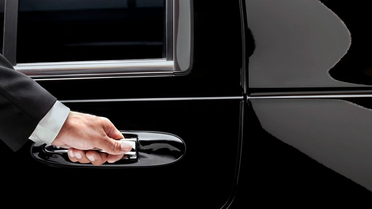 A chauffeur's hand on the door handle of a black car